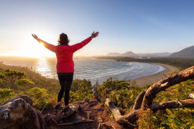 Adventurous Woman Hiker overlooking Sandy Beach on the West Coast of Pacific Ocean. Canadian Nature Landscape Background. Cox Bay Lookout, Tofino, Vancouver Island, BC, Canada.