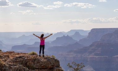 Adventurous Traveler standing on Desert Rocky Mountain American Landscape. Cloudy Sunny Sky. Grand Canyon National Park, Arizona, United States. Adventure Travel