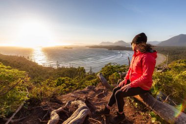 Adventurous Woman Hiker overlooking Sandy Beach on the West Coast of Pacific Ocean. Canadian Nature Landscape Background. Cox Bay Lookout, Tofino, Vancouver Island, BC, Canada.