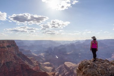 Adventurous Traveler standing on Desert Rocky Mountain American Landscape. Cloudy Sunny Sky. Grand Canyon National Park, Arizona, United States. Adventure Travel