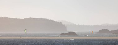 Waves on the Pacific Ocean on a sandy and rocky beach with kitesurfer surfing. West Coast. Sunny Summer. Cox Bay, Tofino, Vancouver Island, BC, Canada.