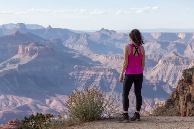 Adventurous Traveler standing on Desert Rocky Mountain American Landscape. Cloudy Sunny Sky. Grand Canyon National Park, Arizona, United States. Adventure Travel