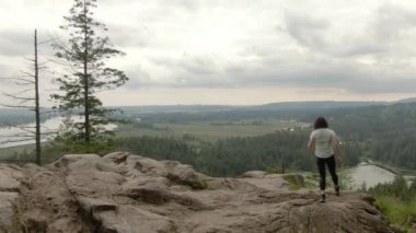 Adventurous Woman Standing on top of a rock overlooking the Canadian Nature Landscape. Minnekhada Regional Park, Coquitlam, Vancouver, British Columbia, Canada.