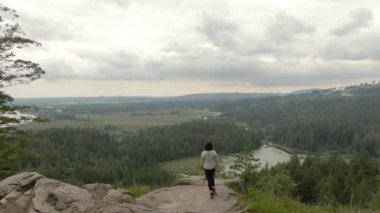 Adventurous Woman Standing on top of a rock overlooking the Canadian Nature Landscape. Minnekhada Regional Park, Coquitlam, Vancouver, British Columbia, Canada.