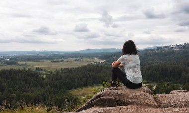 Adventurous Woman Standing on top of a rock overlooking the Canadian Nature Landscape. Minnekhada Regional Park, Coquitlam, Vancouver, British Columbia, Canada.