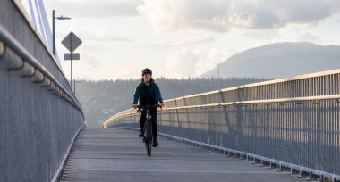 Caucasian Woman riding on a bicycle on a bike lane at Port Mann Bridge. Greater Vancouver, British Columbia, Canada.