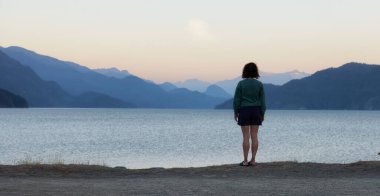 Adventure Woman looking at Harrison Lake during Sunny Summer Morning Sunrise. Canadian Nature Landscape Background. Harrison Hot Springs, British Columbia, Canada. Travel Concept