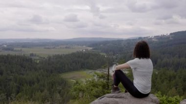 Adventurous Woman Standing on top of a rock overlooking the Canadian Nature Landscape. Minnekhada Regional Park, Coquitlam, Vancouver, British Columbia, Canada.