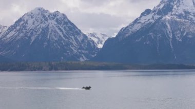 Amerikan arazisindeki ağaçlar ve dağlarla çevrili bir tekne ve göl. Bahar sezonu. Jackson Lake, Grand Teton Ulusal Parkı. Wyoming, Birleşik Devletler. Doğa Arkaplanı. Yavaş Hareket
