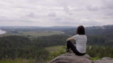 Adventurous Woman Standing on top of a rock overlooking the Canadian Nature Landscape. Minnekhada Regional Park, Coquitlam, Vancouver, British Columbia, Canada.
