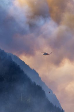 Sıcak bir yaz günü, Hope yakınlarındaki dağda, BC Orman Yangını ve Dumanı 'nın üzerinde uçan Wildfire Servis Helikopteri. British Columbia, Kanada. Doğal Felaket