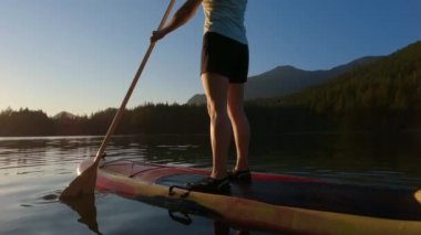 Huzurlu bir gölde kürek çeken maceraperest bir kadın. Güneşli Günbatımı. Hicks Lake, Sasquatch İl Parkı Harrison Hot Springs, British Columbia, Kanada yakınlarında. Yavaş Hareket