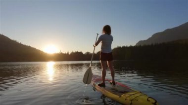 Huzurlu bir gölde kürek çeken maceraperest bir kadın. Güneşli Günbatımı. Hicks Lake, Sasquatch İl Parkı Harrison Hot Springs, British Columbia, Kanada yakınlarında. Yavaş Hareket