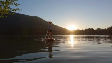 Huzurlu bir gölde kürek çeken maceraperest bir kadın. Güneşli Günbatımı. Hicks Lake, Sasquatch İl Parkı Harrison Hot Springs, British Columbia, Kanada yakınlarında. Yavaş Hareket