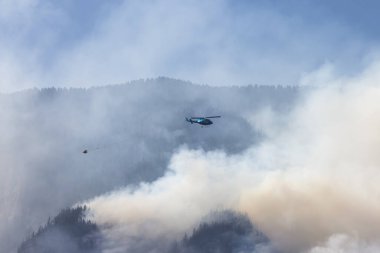 Sıcak bir yaz günü, Hope yakınlarındaki dağda, BC Orman Yangını ve Dumanı 'nın üzerinde uçan Wildfire Servis Helikopteri. British Columbia, Kanada. Doğal Felaket