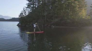 Huzurlu bir gölde kürek çeken maceraperest bir kadın. Güneşli Günbatımı. Hicks Lake, Sasquatch İl Parkı Harrison Hot Springs, British Columbia, Kanada yakınlarında. Yavaş Hareket
