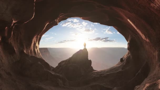 ロッキー山脈を背景にした洞窟の中に立つ冒険的な男ハイカー アドベンチャー コンポジット 3Dレンダリングピーク 背景アメリカの風景画像 サンセット 曇りの空 — ストック動画
