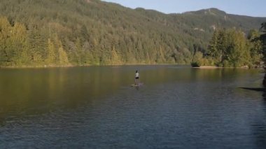 Huzurlu bir gölde kürek çeken maceraperest bir kadın. Güneşli Günbatımı. Hicks Lake, Sasquatch İl Parkı Harrison Hot Springs, British Columbia, Kanada yakınlarında. Yavaş Hareket