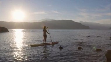 Huzurlu bir gölde kürek çeken maceraperest bir kadın. Güneşli Günbatımı. Harrison Kaplıcaları, British Columbia, Kanada. Macera Sporu Seyahat Konsepti. Yavaş Sinema Sineması
