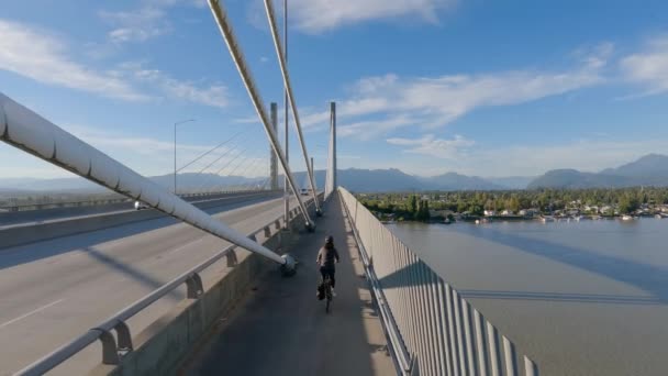 フレイザー川にかかる黄金の耳の橋の上の自転車道に乗っている女性の自転車 ピット メドウズ ラングレー グレーターバンクーバー ブリティッシュコロンビア州 カナダ 高品質4K映像 — ストック動画