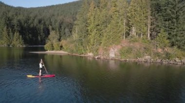 Huzurlu bir gölde kürek çeken maceraperest bir kadın. Güneşli Günbatımı. Hicks Lake, Sasquatch İl Parkı Harrison Hot Springs, British Columbia, Kanada yakınlarında. Yavaş Hareket