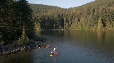 Huzurlu bir gölde kürek çeken maceraperest bir kadın. Güneşli Günbatımı. Hicks Lake, Sasquatch İl Parkı Harrison Hot Springs, British Columbia, Kanada yakınlarında. Yavaş Hareket