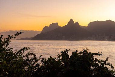 Ipanema, Rio de Janeiro, Brezilya 'da okyanus, dağlar ve turuncu gökyüzü ile güzel sahil gün batımı manzarası