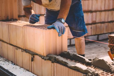 Professional construction worker laying bricks and mortar - building external house walls. Construction site detail -closeup of hand adjusting bricks