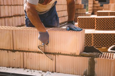 Professional construction worker laying bricks and mortar - building external house walls. Construction site detail -closeup of hand adjusting bricks