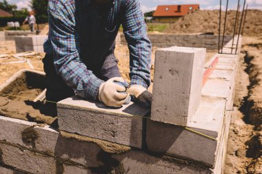 Professional construction worker laying bricks and mortar - building external house walls. Construction site detail -closeup of hand adjusting bricks