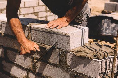 Professional construction worker laying bricks and mortar - building external house walls. Construction site detail -closeup of hand adjusting bricks