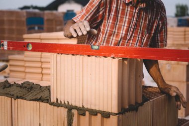 Professional construction worker laying bricks and mortar - building external house walls. Construction site detail -closeup of hand adjusting bricks