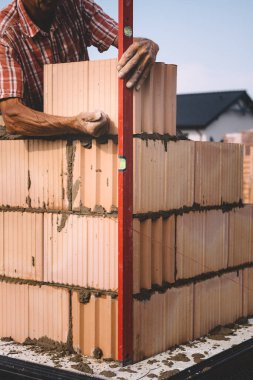 Professional construction worker laying bricks and mortar - building external house walls. Construction site detail -closeup of hand adjusting bricks