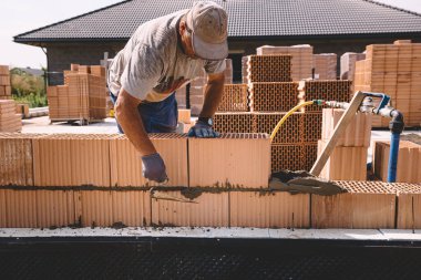 Professional construction worker laying bricks and mortar - building external house walls. Construction site detail -closeup of hand adjusting bricks