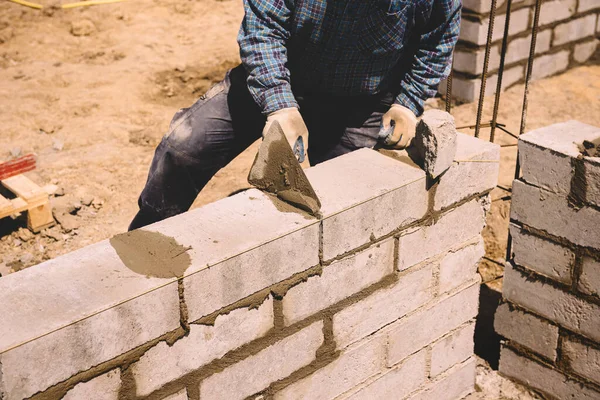 Professional construction worker laying bricks and mortar - building external house walls. Construction site detail -closeup of hand adjusting bricks