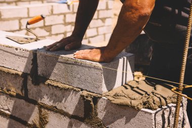 Professional construction worker laying bricks and mortar - building external house walls. Construction site detail -closeup of hand adjusting bricks