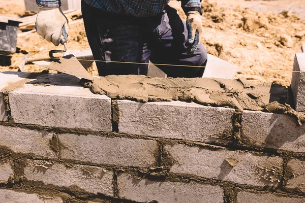 Professional construction worker laying bricks and mortar - building external house walls. Construction site detail -closeup of hand adjusting bricks