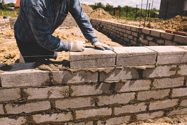 Professional construction worker laying bricks and mortar - building external house walls. Construction site detail -closeup of hand adjusting bricks