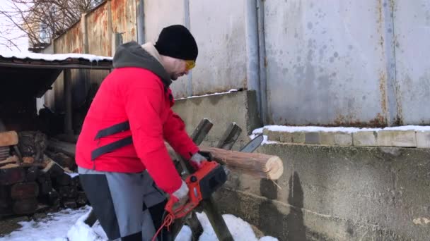 A man saws logs using an electric saw. Outdoor shot on a winter day. — Stock Video