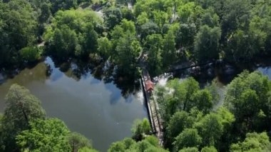 Dron gezisi. Yeşil çam ormanının üzerinde hızla uçuyor, ahşap köprüsü ve kemeri olan nehir, park alanı, yol ve tramvay kazıkları..