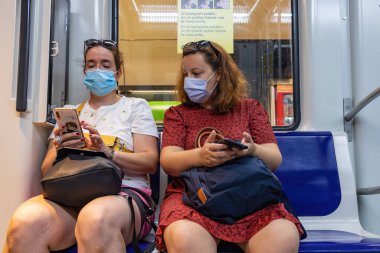 Barselona, İspanya - 21 Eylül 2021: İki kadın metroda seyahat ederken cep telefonunu kullanıyor. Koronavirüs covid-19 salgınından dolayı koruyucu yüz maskesi kullanıyorlar.