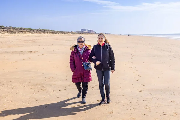 一个成熟的女人和她年老的母亲在海滩边散步 — 图库照片