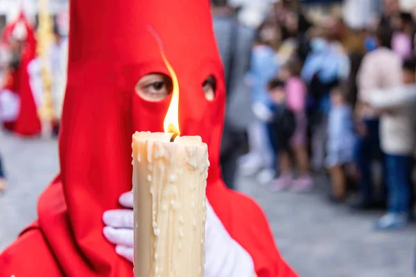 一个年轻的拿撒勒人的点燃着的蜡烛 他戴着红色的帽子 在圣周的游行中做他的忏悔站 选择焦点 只有焦点上的烛焰 — 图库照片
