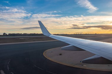 Uçak gün batımında havaalanına indiğinde yolcu koltuğunun penceresinden uçak kanadının görüntüsü.