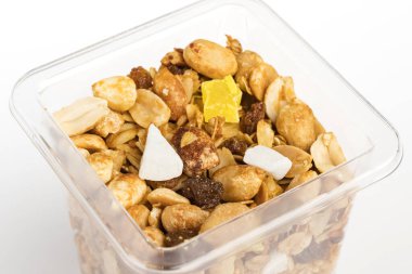 Fındıklı gevrek ve kurutulmuş meyve. Beyaz arka planda açık plastik kapta ev yapımı müsli.