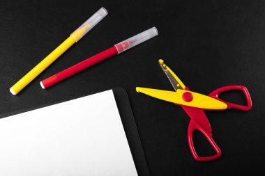 Siyah bir masaüstünde kıvırcık kesim için makaslı kırmızı ve sarı işaretler. Uzayı metin için kopyala. Okul ve yaratıcılık için kırtasiye konsepti. Üst görünüm