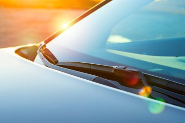 Gün batımında parlak güneşin parladığı bir arabanın ön camında fırçalar. Temizlik ürünleri, cilalama, yağmur önleme kavramı