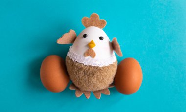 Mavi arka planda oyuncak tavuk ve iki yumurta..