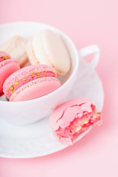 Rosa und cremefarbene Macarons in einer weißen Porzellantasse auf rosa Hintergrund — Stockfoto