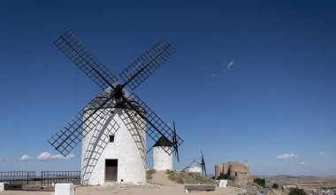 Konsuegra, Toledo, Castilla La Mancha, İspanya 'daki yel değirmenleri ve eski şato. Birkaç yel değirmeni ve kale küçük bulutlu bir gökyüzünün altında bir tepede.